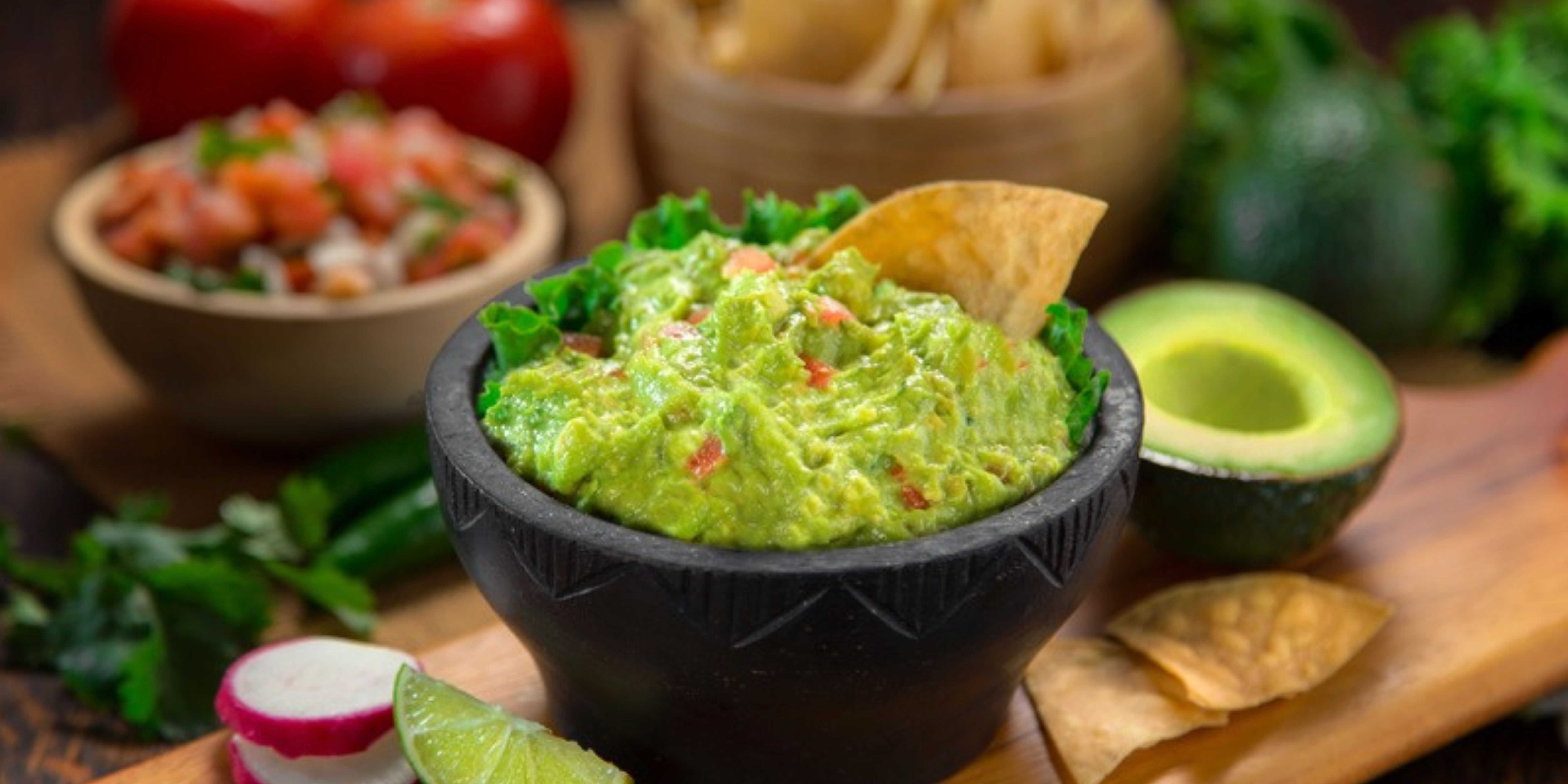 Fresh guacamole in a black molcajete with avocado, salsa, and tortilla chips