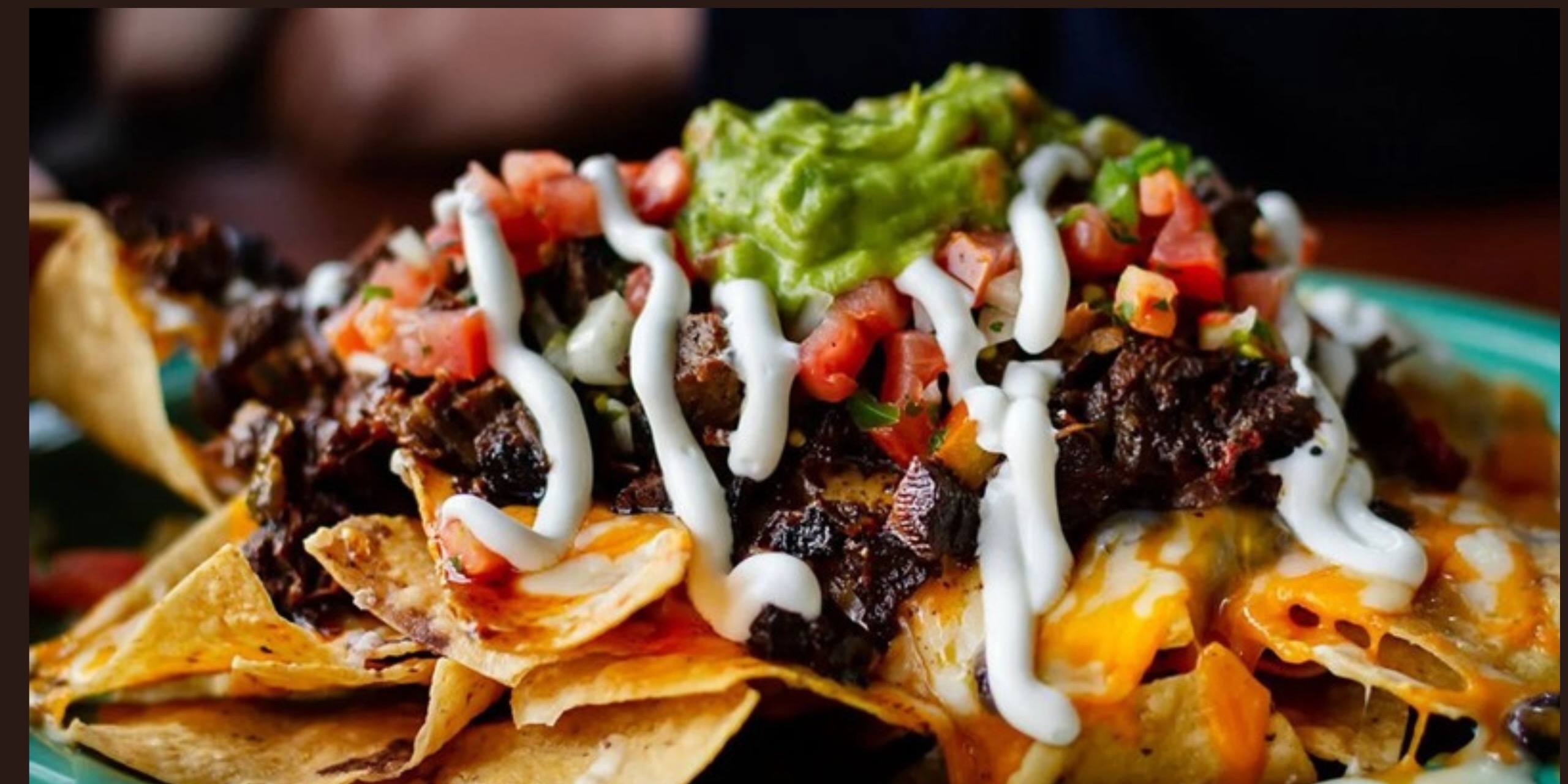 Loaded nachos with melted cheese, meat, pico de gallo, guacamole, and crema